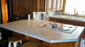 Una cocina con armarios de madera, una isla grande con taburetes, un fregadero y una ventana con persianas.