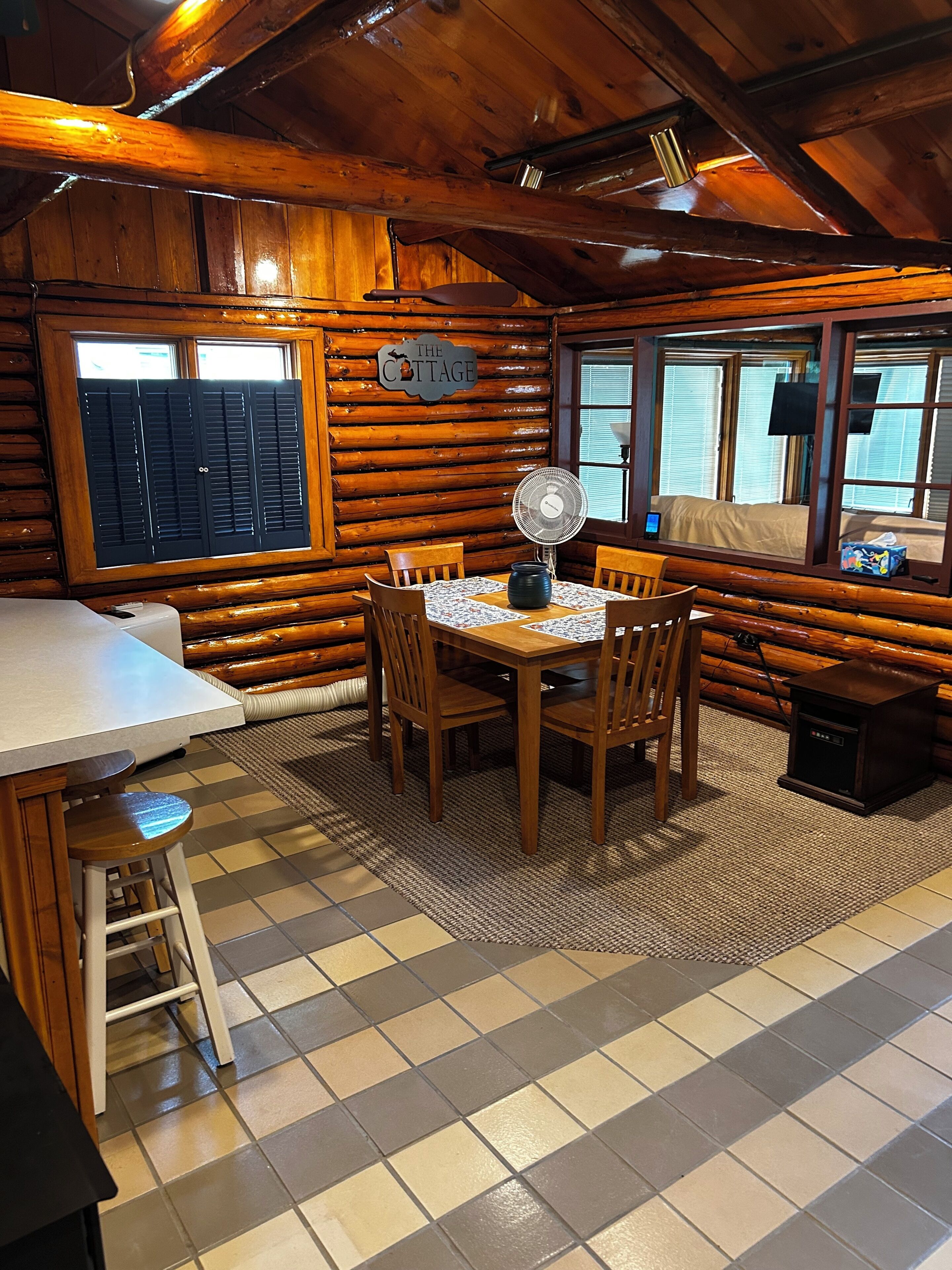 L’intérieur d’une cabane en rondins, avec une table à manger, des chaises, un ventilateur et une petite table d’appoint.