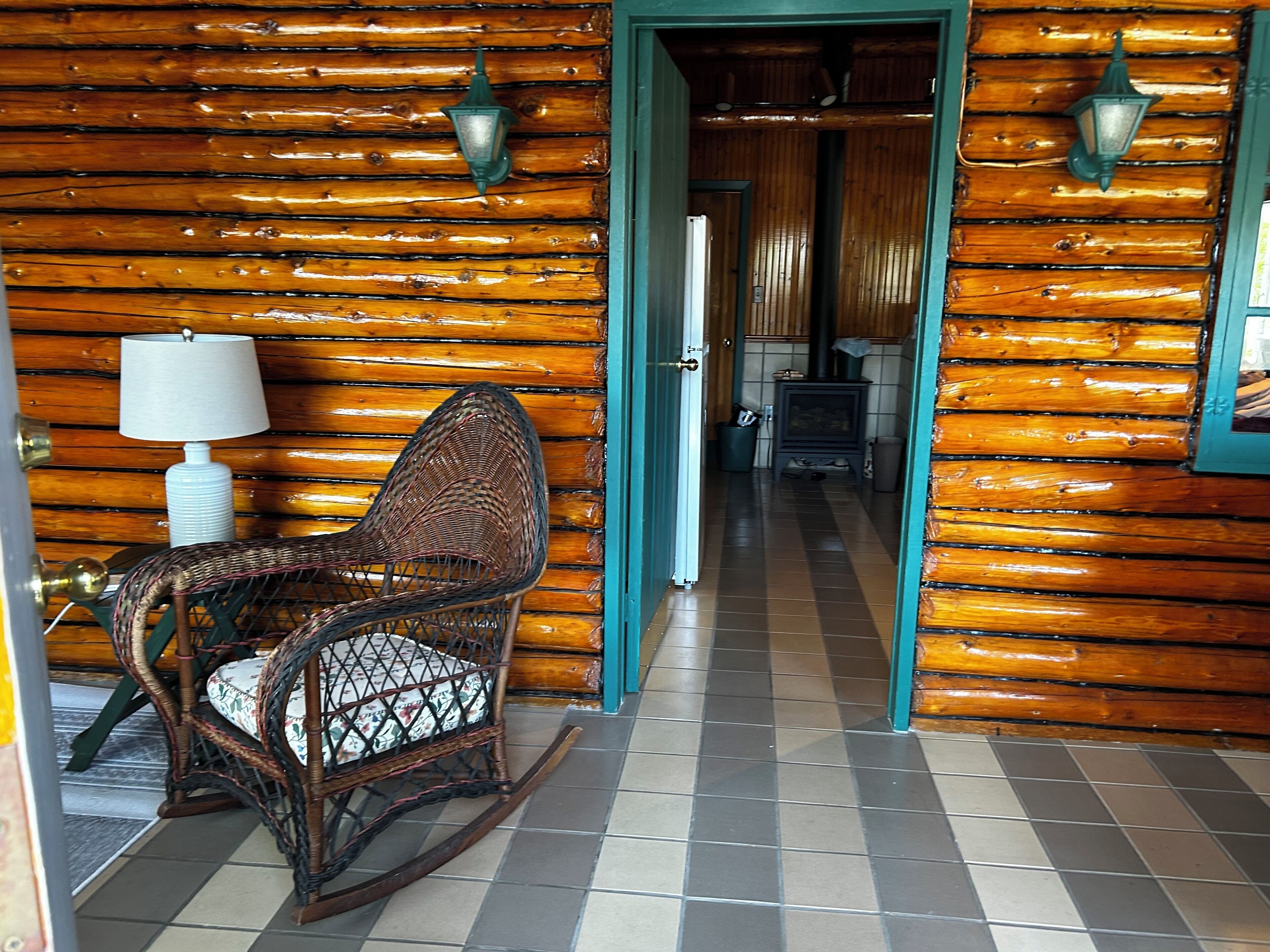L’intérieur d’une cabane en rondins, avec un fauteuil à bascule, une lampe et une cheminée.