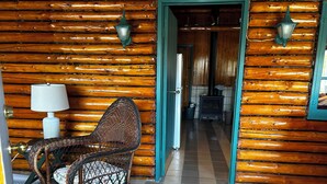 Interior de una cabaña de troncos con una mecedora, una lámpara y una chimenea.