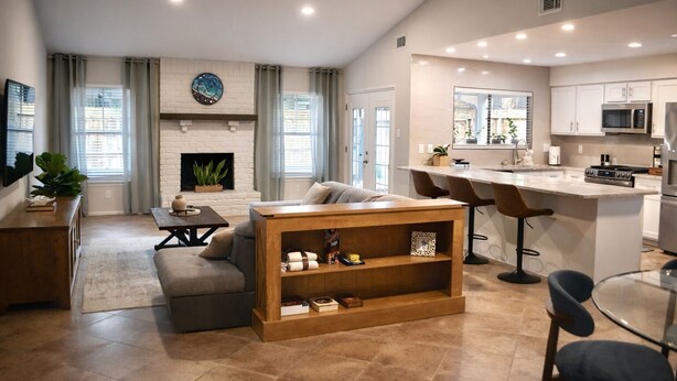 A modern living room with a fireplace, a sofa, a coffee table, and a kitchen area with a bar and seating.