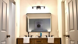 A bathroom with wooden cabinets, a mirror, and two white rugs on the floor.
