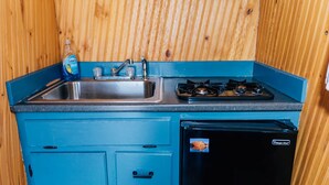 A compact kitchen with a sink, faucet, and stove, and a black refrigerator. - Farmside Tiny Home (Lyman)