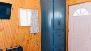 A room with wooden walls, a blue cabinet, a white door with a window, and a small window with a curtain. - Farmside Tiny Home (Lyman)