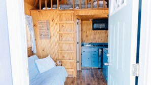 A cabin interior with a bed, a wooden ladder, a kitchen area, and a sign listing cabin rules. - Farmside Tiny Home (Lyman)
