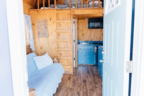 A cabin interior with a bed, a wooden ladder, a kitchen area, and a sign listing cabin rules.