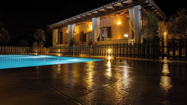 Una vista notturna di una casa con piscina, patio coperto e recinzione.