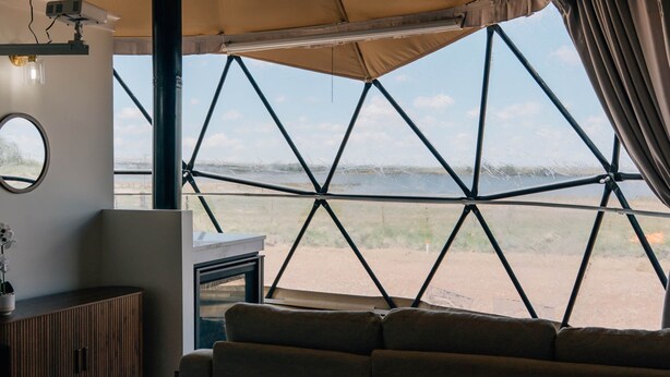 Ein Zelt mit geometrischem Fensterdesign, einer Couch, einem kleinen Tisch und einem Kamin.