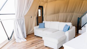 Ein Zeltraum mit einem weißen Sofa, Holzboden und einer Treppe.