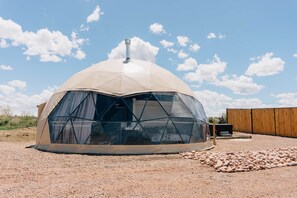 Una estructura de domo geodésico con un lateral transparente, una chimenea y suelo de grava.