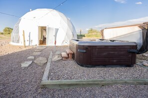 A geodesic dome structure with an open door, a hot tub, and a wooden bench. - White Geodome Ranch Retreat- With a Hot Tub! (Lyman)