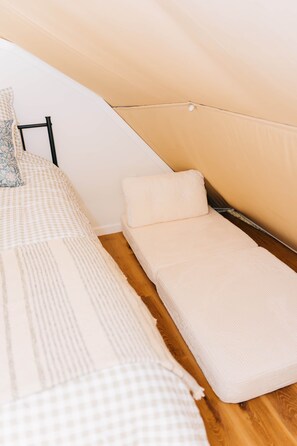 Une petite chambre avec un lit simple, une couverture à carreaux, un matelas sobre et un plancher en bois.