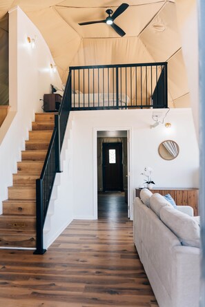 A staircase leading to a second floor, a ceiling fan, a wooden staircase, a white wall, a mirror, and a sofa.