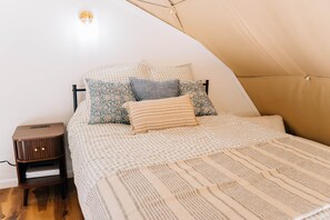 Een gezellige slaapkamer met een bed, kussens, een nachtkastje en een wandlamp.