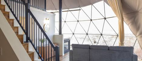 A spacious interior with a wooden staircase, a gray sofa, and a large tent-like structure with a geometric pattern.