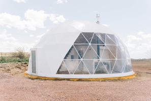 A geodesic dome structure with a transparent window section, a door, and a chimney.