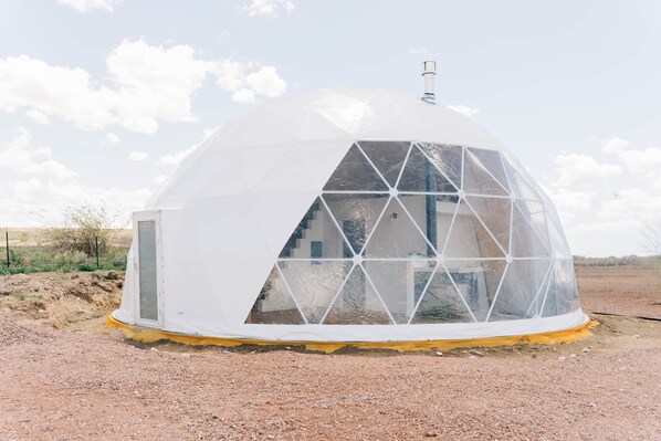 A geodesic dome structure with a transparent window section, a door, and a chimney.