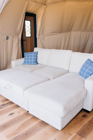 Een witte, modulaire bank met blauwe kussens in een tentachtige ruimte met houten vloeren.