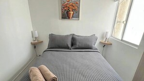 A neatly made bed with a grey quilt, two pillows, and two rolled towels on the bed. There is a painting of flowers on the wall above the bed. - MARETA TORICES HOUSE (Cartagena de Indias)