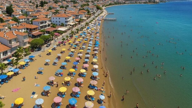 Un pueblo costero con una playa bordeada de sombrillas y tumbonas, un muelle que se adentra en el mar y edificios residenciales a lo largo de la orilla.
