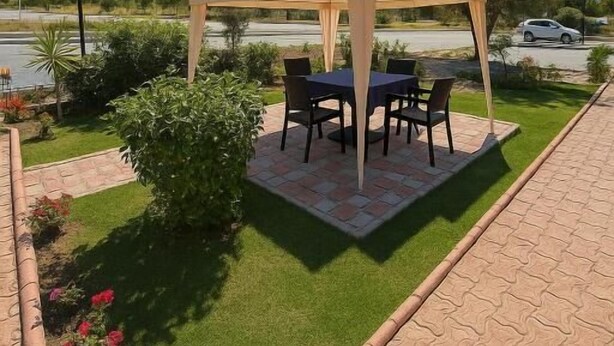 A covered outdoor seating area with a table and chairs, surrounded by a well-maintained garden with grass and plants. - HOTEL PANORAMA ÖZDERE (Menderes)