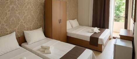 Quarto de hotel com duas camas, um guarda-roupa, uma mesa de trabalho e uma janela com cortinas.