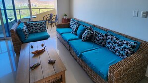 Een woonkamer met een rieten bank, een houten salontafel en uitzicht op een balkon.