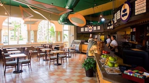 A restaurant with a checkered floor, wooden tables and chairs, a counter with food items, and a menu board. - Cabo 3BR Presidential – Beach, Pools & Oceanfront Stay (Cabo San Lucas)