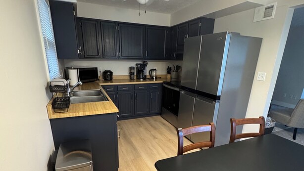 Una cocina moderna con armarios oscuros, un refrigerador de acero inoxidable, una cafetera y una mesa de comedor con sillas.