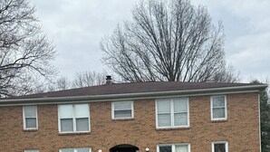 Un edificio de apartamentos de ladrillo de dos pisos, con entrada central, un pequeño jardín delantero y un camino de acceso pavimentado.
