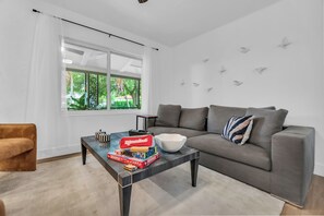 Una sala de estar moderna con un sofá gris, una mesa de centro con juegos de mesa y un ventanal con vistas a zonas verdes.