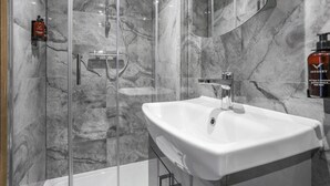 A modern bathroom with a glass-enclosed shower, a white sink, and marble walls. - Central London 1-Bed Flat – Hyde Park & Paddington Area (London)