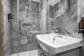 A modern bathroom with a glass-enclosed shower, a white sink, and marble walls. - Central London 1-Bed Flat – Hyde Park & Paddington Area (London)