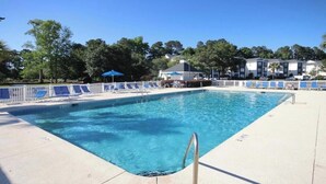 Una piscina rectangular con una escalera de metal, rodeada por una valla blanca y sillas de descanso azules.