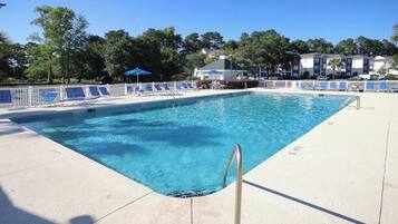 A rectangular swimming pool with a metal ladder, surrounded by a white fence and blue lounge chairs.