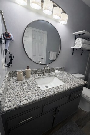 A bathroom with a granite countertop, a sink, a mirror, a hairdryer, and a towel rack. - Gorgeous 3-bedroom condo perfect for your stay in lively Myrtle Beach! (Myrtle Beach)
