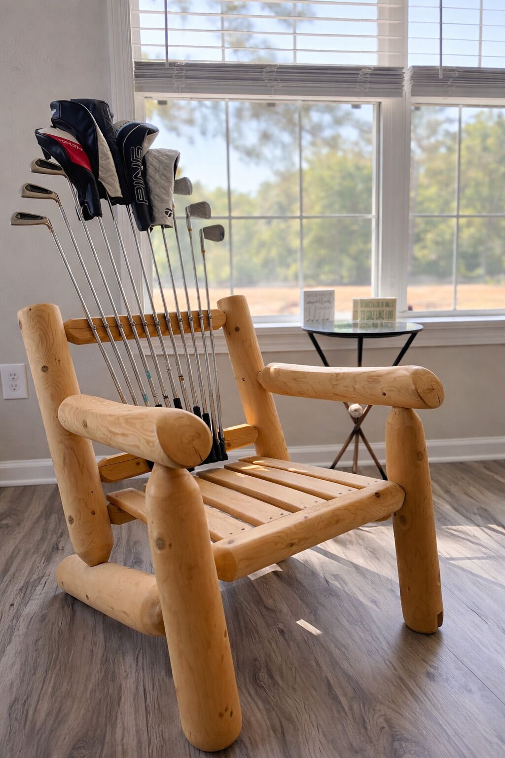 A wooden chair with metal golf clubs leaning against it, positioned in a room with a large window and a small table.