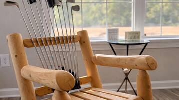 A wooden chair with metal golf clubs leaning against it, positioned in a room with a large window and a small table.