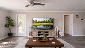 Una sala de estar con televisor, una mesa de centro, una planta en maceta y una puerta.