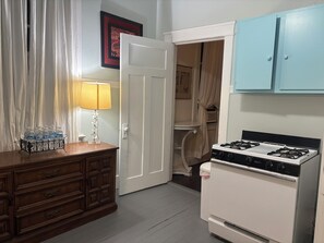 A kitchen with a stove, a wooden cabinet, a water dispenser, and a door leading to a closet. - 2-bedroom shotgun house in lovely New Orleans with historic charm (New Orleans)