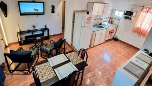 Un espace de vie compact comprenant un coin repas, une cuisine et un téléviseur fixé au mur.
