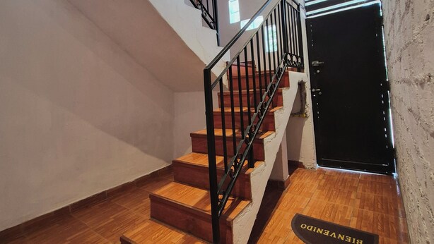 Un escalier avec des marches en bois et des rampes en métal noir, menant à une porte dotée d’une poignée noire.
