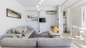 Uma sala de estar moderna com um sofá seccional cinza, uma televisão de tela plana, uma mesinha de centro e uma janela grande.
