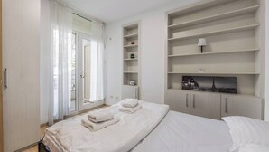 Quarto com cama, guarda-roupa, prateleira embutida com abajur e janela com cortinas.