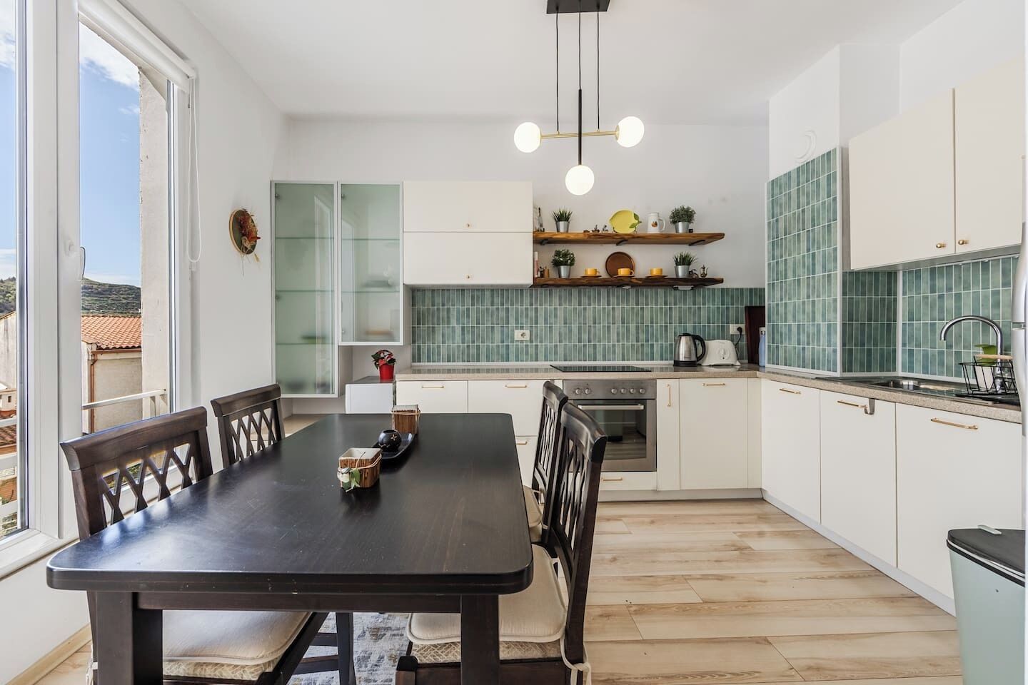 A modern kitchen with a dining table, chairs, a hanging light fixture, and a view of the outside.