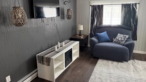 A living room with a grey wall, a flat-screen TV, a fireplace, a sofa, and a window with curtains. - Quiet Place Close to Utica, Cooperstown, Thruway, and NYS Canal Trail (Mohawk)