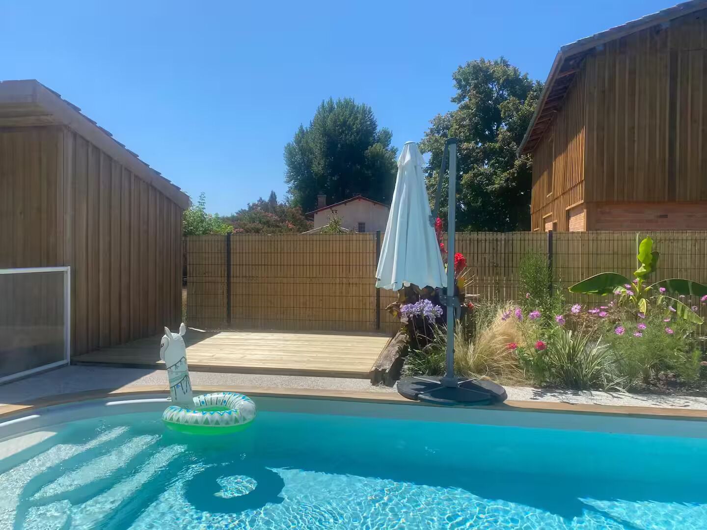 A backyard with a swimming pool, a wooden deck, and a fenced area.