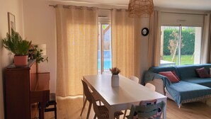 Un comedor con una mesa y sillas blancas, una lámpara colgante y un sofá con cojines.