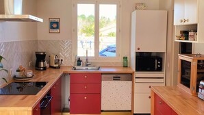 Una cocina moderna con una isla central, armarios rojos, lavavajillas integrado y un amplio ventanal con vistas al exterior.