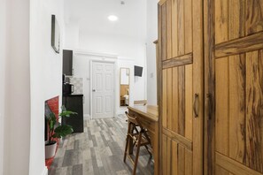 Un couloir avec une porte en bois, une table à manger avec des chaises, une plante en pot et un réfrigérateur.